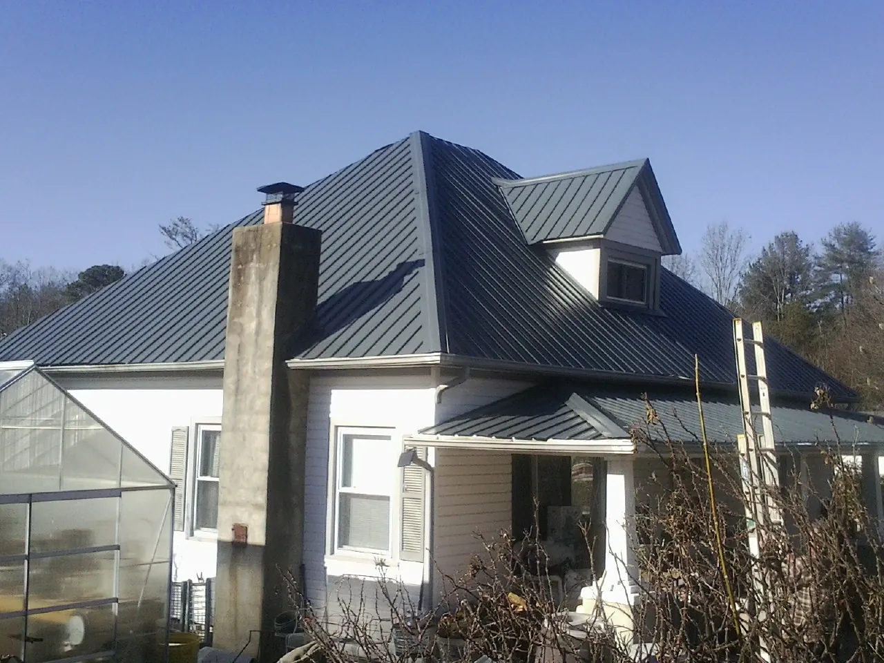 Dark blue standing seam metal roof on a white farmhouse with dormer — Slate & Tile Roof Repair by Roofing Brothers in Pinckney
