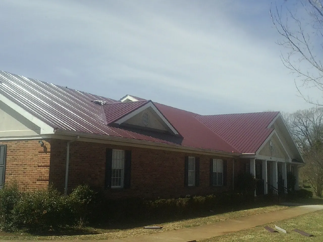 Red metal roof with gabled entries on a long brick building, from a Hail Damage Roof Repair job in Pinckney