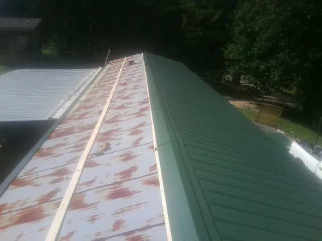 Old rusted panels beside newly installed green metal roofing — Wind Damage Roof Repair by Roofing Brothers in Pinckney