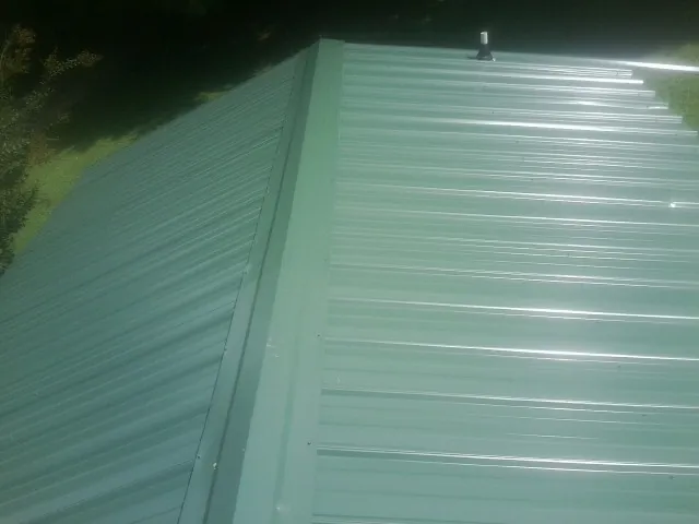 New green metal panels meeting at the ridge of a roof — Flat Roof Repair work by our crew in Pinckney