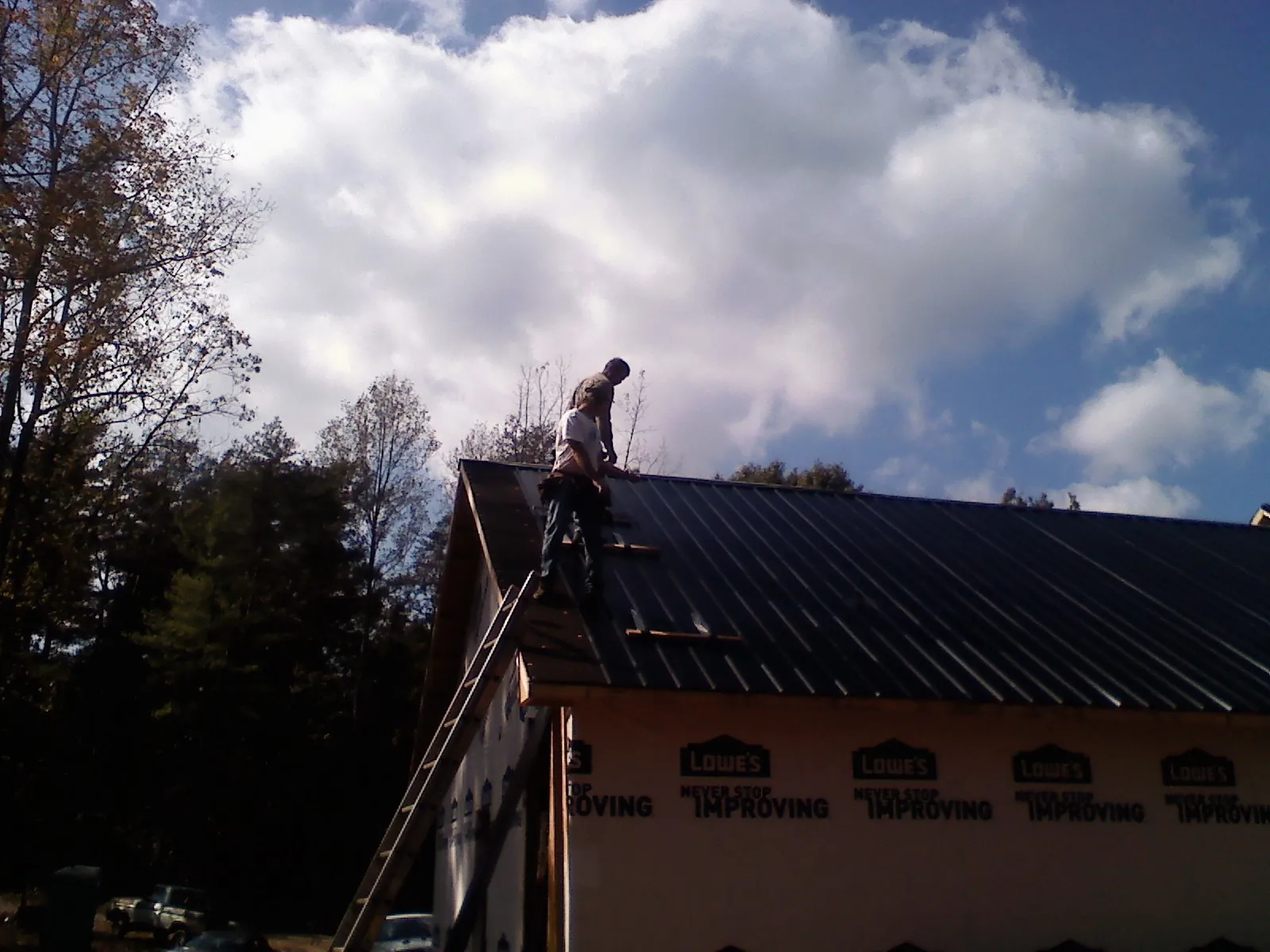 Roofer fastening dark metal panels high against a cloudy sky, from a Roof Inspection job in Pinckney