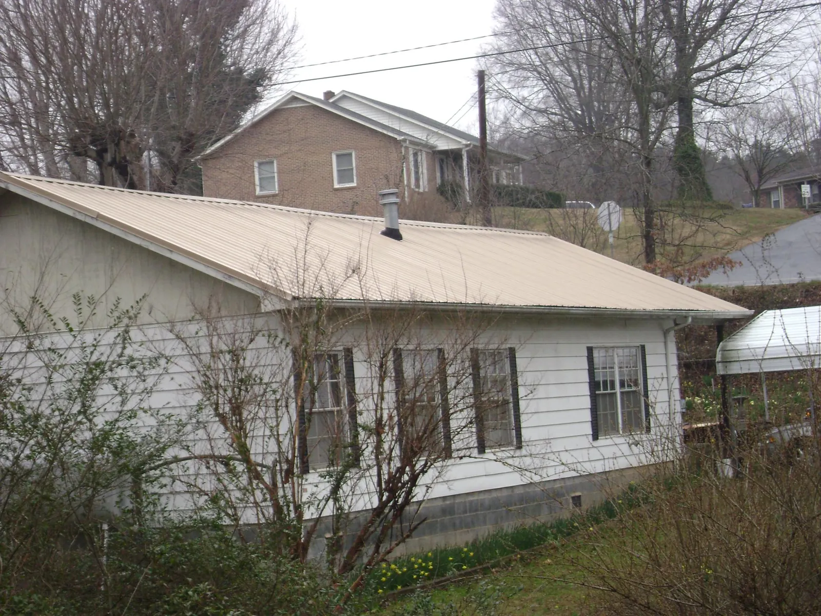 Tan metal roof on a white sided house set into a hillside — Commercial Roofing by Roofing Brothers in Pinckney